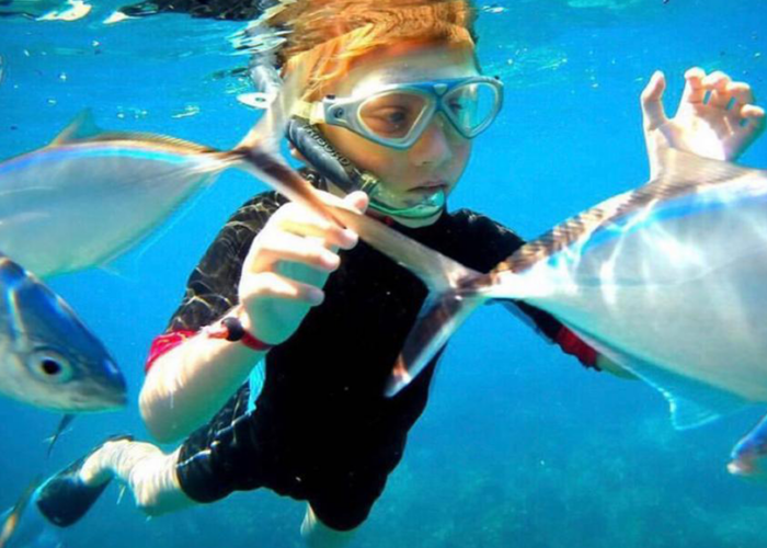 Child snorkeling with fish in clear waters of Punta Cana, a top destination for excursions.
