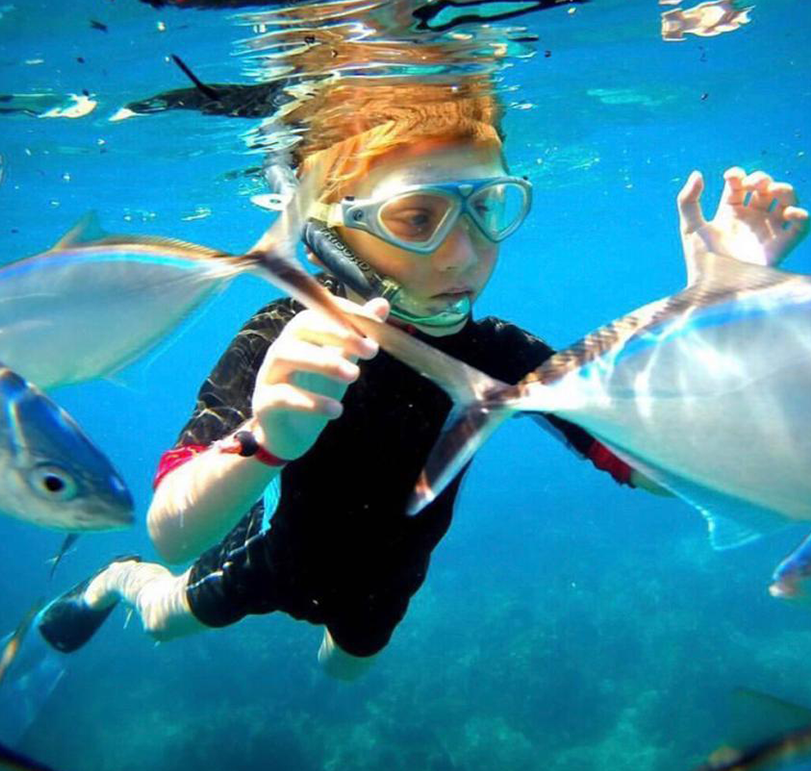 Child snorkeling with fish in clear waters of Punta Cana, a top destination for excursions.
