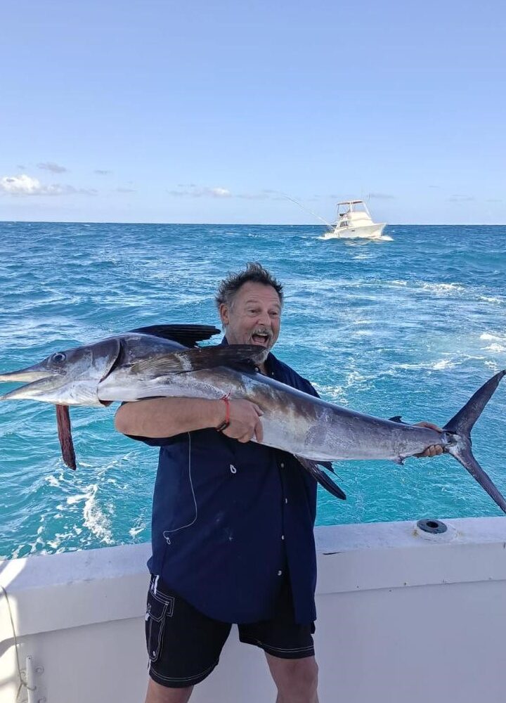 Man holding a large marlin while fishing in Punta Cana waters with a boat in the background.