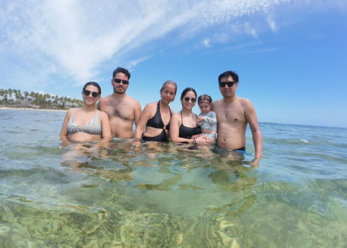 Family enjoying a sunny day in Punta Cana's clear waters with palm trees in the background.